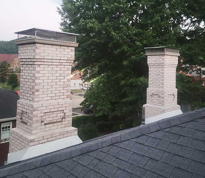 Two white masonry chimney after restoration with trees and buildings in the background.