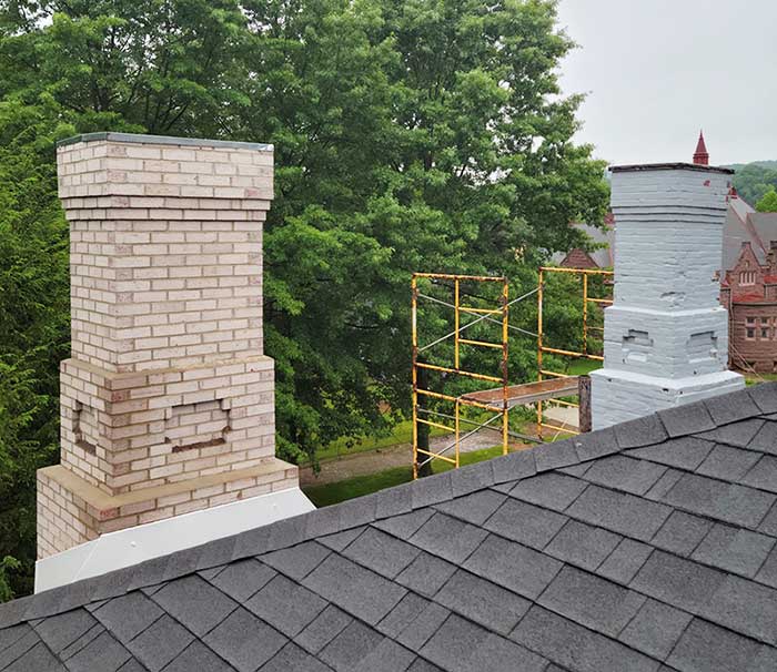 Original photo of before and after chimney redesign - Top Cat Chimney - Cowansville, PA Chimney with insert design in brick before it is cream colored and after it is white with scaffolding and trees along with a building in the background