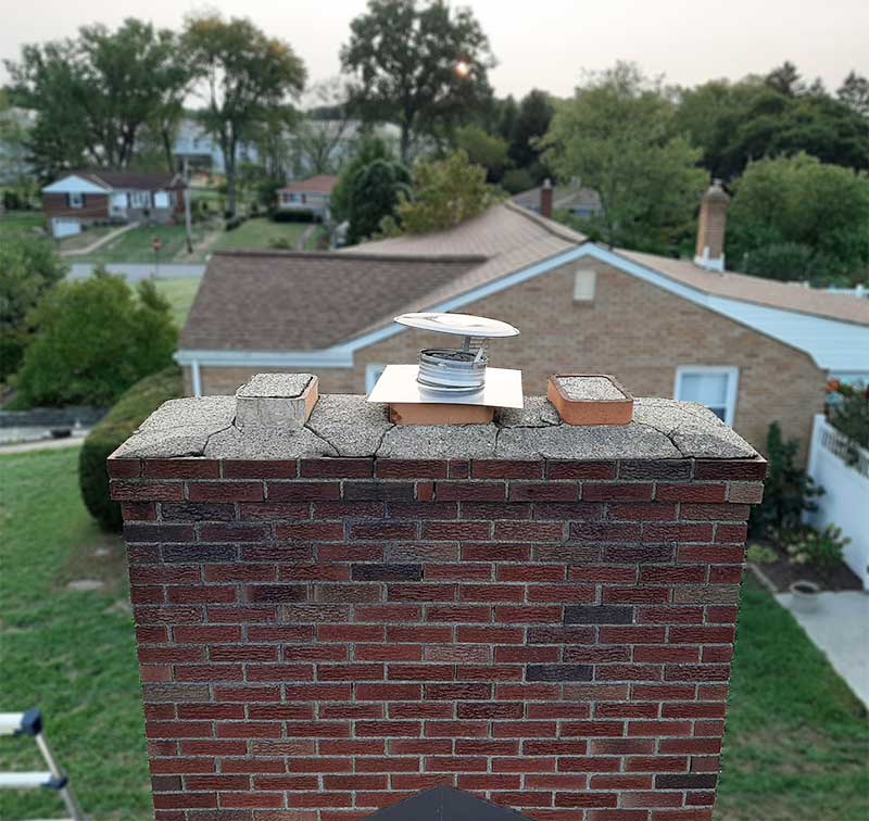 Masonry chimney with a crumbling chimney crown before restoration - homes and trees in the background