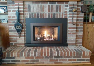 New gas insert with black facing multi-colored brick surround with wooden mantel tools on each sdie bookcase on the left and cabinet on the right.