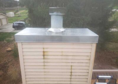 Stainless steel chase cover after replacement with a tree car and garage in the background - ladder in the foreground.