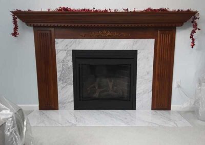 Beautiful gas fireplace insert surround by marble and wood with wood mantel decorated for Christmas and a marble hearth.
