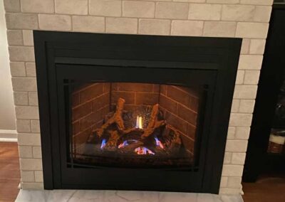 New gas insert with black facing and white brick surround with marble hearth and wooden flooring.