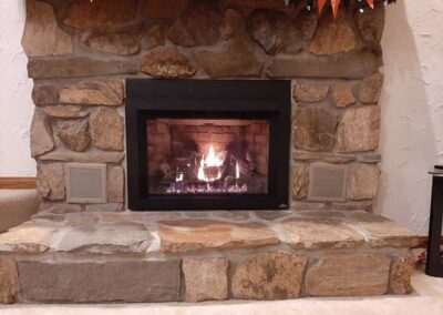 New gas fireplace insert with black facing and sculpted rock surround and hearth with venting on each side.