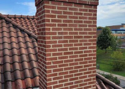 Tall masonry Chimney on tile roof with building in the background.