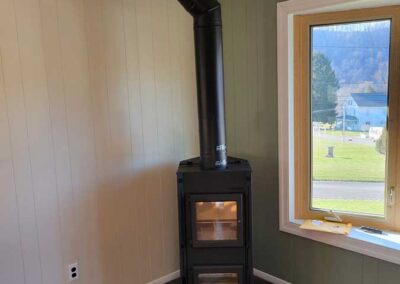 Corner freestanding pellet stove large window to the right and wood flooring