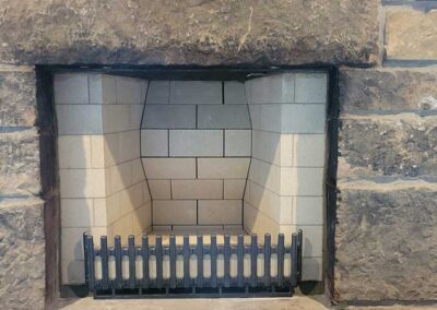 PriorFire Firebox before sweeping with beautiful curvy lines made with white fire bricks a rock hearth and a grate in front.