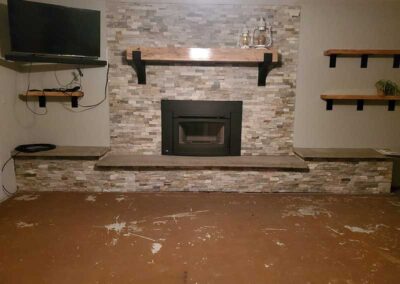 Masonry fireplace after repair with new wood insert - beautiful stone surround and hearth - two wood shelves to the right and a tv mounted to the left.