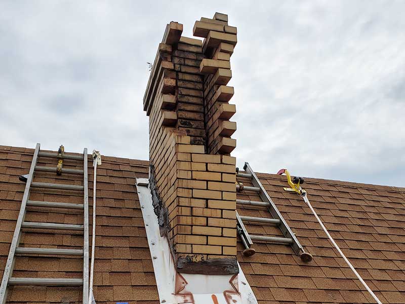 Original image of bricks missing on the front side - Top Cat Chimney - Cowansville, PA Masonry chimney with bricks missing on the front - Ladders on each side and safety gear to the right - clouds in the background