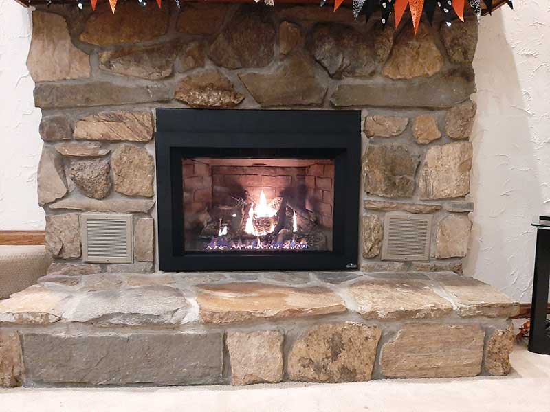 New gas insert with rock backdrop and hearth and a flame in the fireplace.