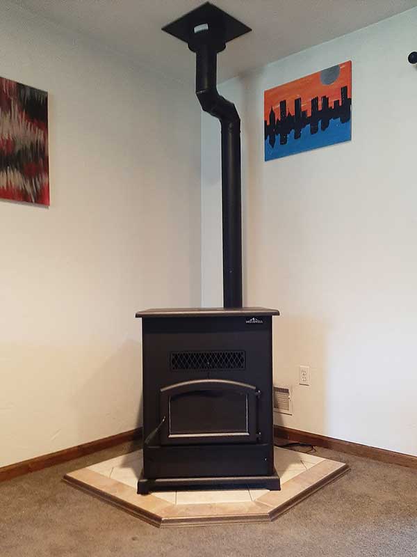 Newly installed wood stove with stove pipe running to the ceiling - tile hearth and modern pictures on white walls.