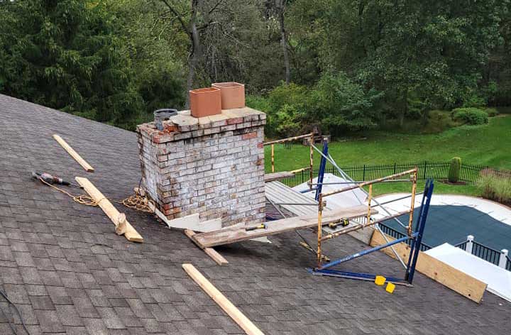 Old chimney on roof being restored - woods in the background as well as a covered pool with a fence around the pool