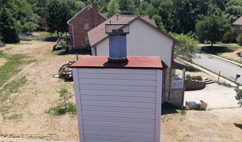 Original image of rusted chase cover - Top Cat Chimney - Cowansville, PA Rusted chase cover on top of chimney - Homes and lots of trees in the background