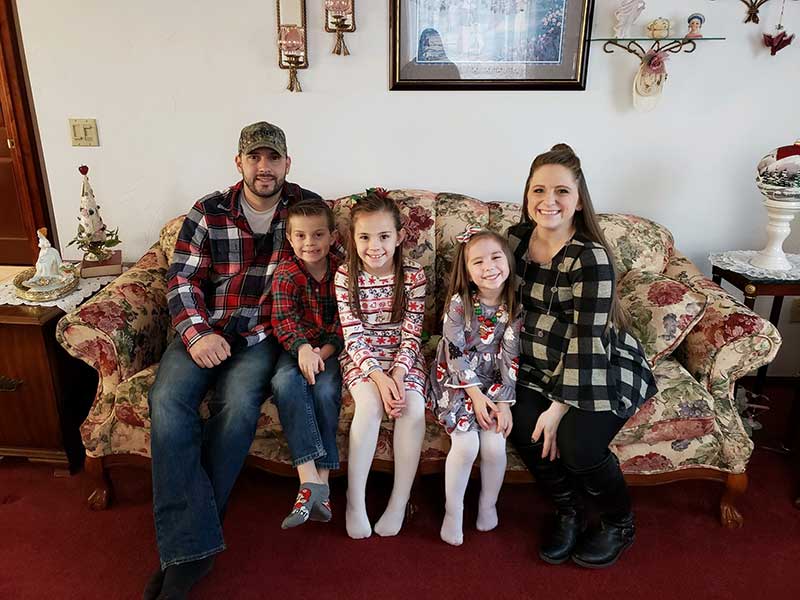 Family of mom and dad owners with two little girls and one little boy sitting on a living room sofa.