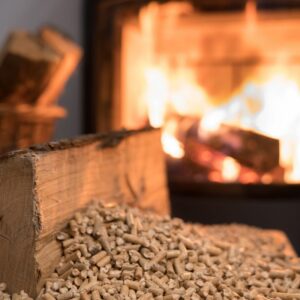 a piece of wood by a bunch of wood pellets with a burning stove in the background