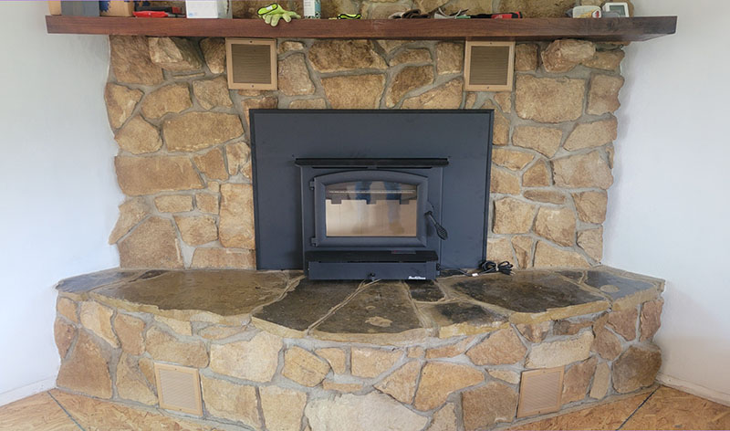 New wood stove with a rock surround and a wooden mantelpiece